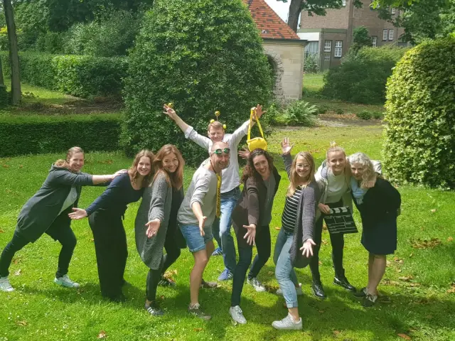 Een groep deelnemers poseert vrolijk samen in de tuin tijdens een praktijkdag teambuilding